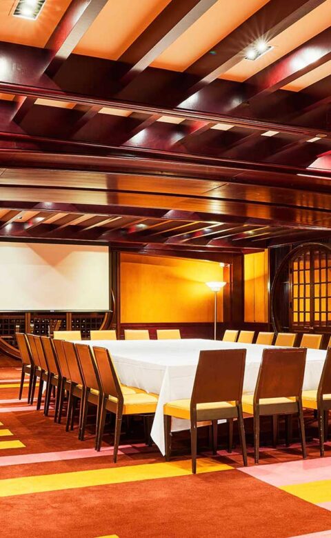 a boardroom set up with chairs around a large rectangular table and a projector screen in the background