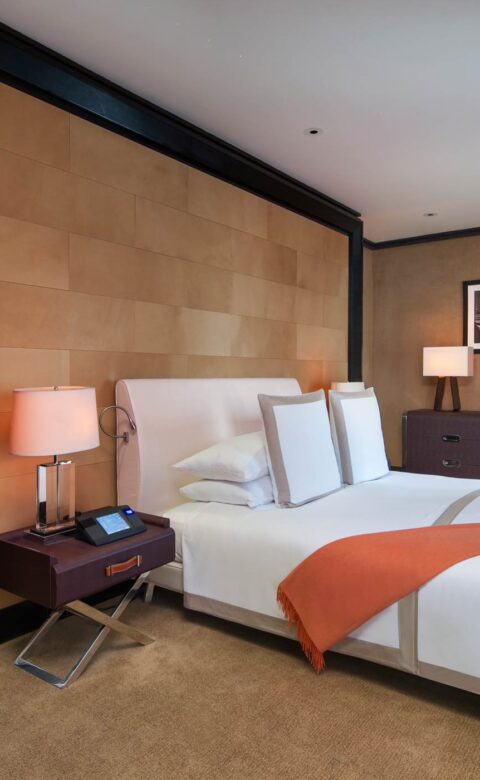 A suite bedroom with a King Size bed with an orange throw, and an entrance to a modern bathroom.