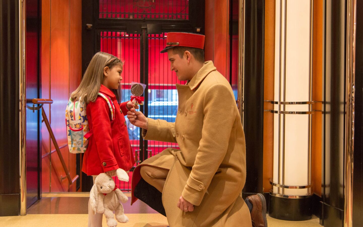 a concierge on his knees giving a girl a chocolate lollipop