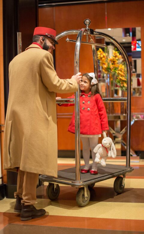 Hotel porter pushing a girl on a suitcase cart